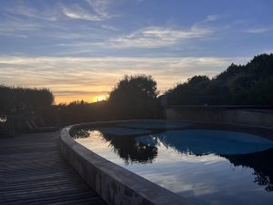 Séjour Corse septembre 2023 - Résidence de vacances Cantu Di Mare. Image représentant au premier plan une piscine, puis au deuxième-plan, des arbres et au loin le coucher du soleil.